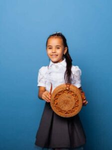cropped-cute-little-girl-of-seven-years-old-posing-in-school-uniform-and-holding-a-wicker-round-bag-on-a-blue-background.jpg